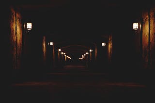 Dark, dimly lit alley with lanterns lighting up patches of the walls.