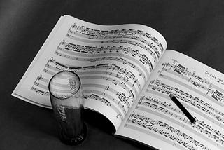 A black and white image of music with a glass next to it.