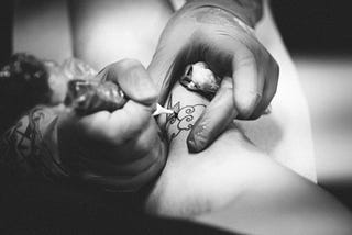 A black and white shot shows a man tattooing.