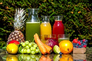 A set up of assorted fruits and what green, orange and beetroot juices and smoothies in transparent bottles.