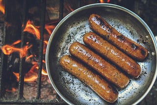 A pan full of cooking sausages on a coal fire grill