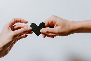 two hands holding a black paper heart