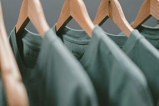 Identical grey tshirts hang from wooden hangers, the same shirt over and over and over.