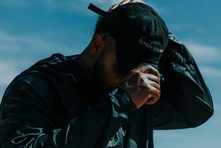 a man outside, wearing a black hat and a black sauna suit, you can see drips of sweat on the outside of the suit on his chest