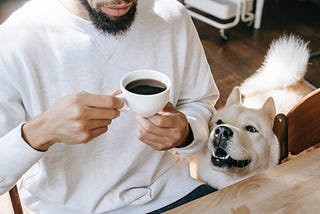 man having black coffee and his dog sitting by him