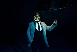 Dude in a fancy suit and a purge mask, holding an umbrella