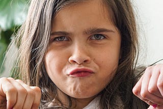 Young girl with brunette hair shows her thumbs down.