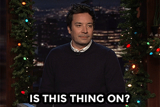 GIF of Jimmy Fallon pretending to tap on a microphone and saying In This Thing On?