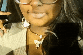 A gif of me from my IG jupiter.dior. I’m wearing a nude top, with a sparkly butterfly necklace, sparkly sun and mood earings, and gold moving butterfly clips in my wig. It’s dark brown with a platinum moneypiece. The filter I am using has gold sparkles cascading down my face. Text says “I got read down today and low key I really needed to hear it 🙃”