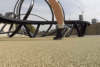 A runners legs in front of a sculptural metal bench in London