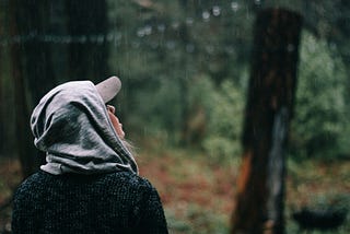 A young woman looks out at the trees in a storm.