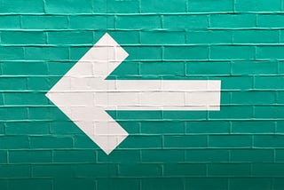 A white arrow pointing leftward on a field of green bricks.