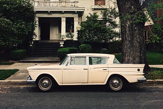 An old-fashioned wooden house with a retro car out front.