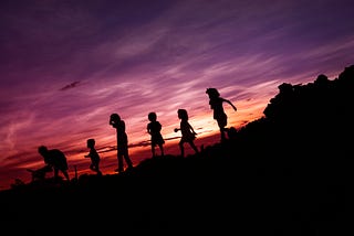 Children running along a hill silhouetted by a purple sunset