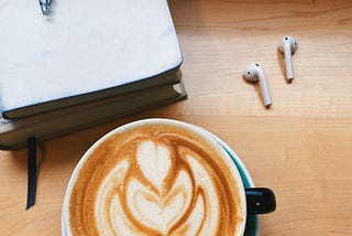 A latte, some earbuds, and a notepad with a pen.
