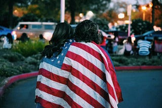 Two people seen from behind wrapped in the American flag.