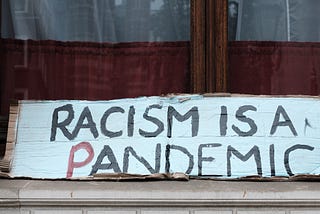 A sign with the text “Racism is a pandemic”
