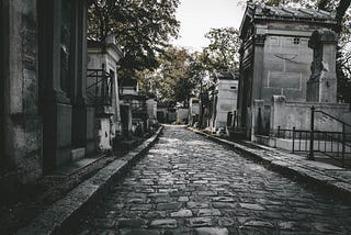 A darkish image of a cobblestone path to a graveyard.