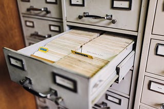 A filing cabinet with an open drawer with many index cards inside.