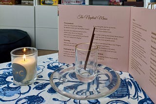 Incense, a candle, and a bound wedding program on a table with a blue and white floral tablecloth.