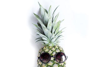 A pineapple with round sunglasses on it, on a white background.