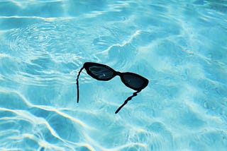 Sunglasses floating in bright blue water.