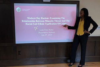 Leah Butler stands in front of a screen that shows her doctoral dissertation, “Modern Day Racism: Examining the Relationship Between Minority Threat and the Racial and Ethnic Typification of Crime.”