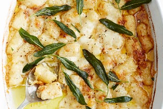 An oval casserole dish of gnocchi gratin garnished with crispy sage leaves.