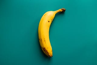 A photo of a banana against a teal background.