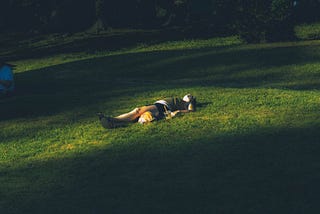 Person laying on their back on a grassy knoll.