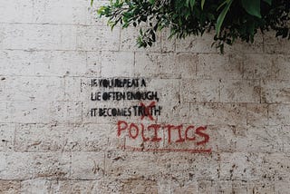 Graffiti quote on a wall saying: If you repeat a lie often enough, it becomes POLITICS.