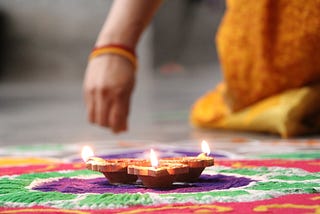 Traditional Indian patterns called ‘rangoli’ being made with colours along with a display of few lit earthen lamps.