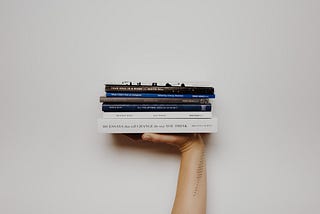A hand holding a stack of books with a simple background.