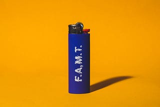 The white Lighter Curse stuck around for a reason by nicole wallet. This photo is of a blue BIC lighter with the letters FAMT on the side. Orange background