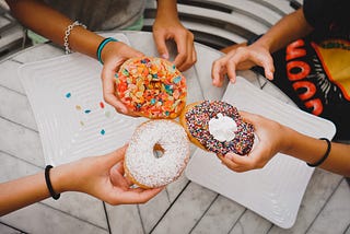 Three sets of hands holding decadent donuts.