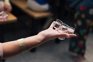 Person holding four shot glasses in one hand.