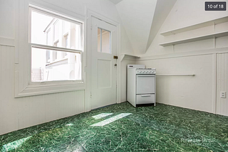 A white oven awkwardly placed in the corner of an otherwise empty room with green vinyl flooring.