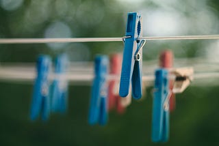 One in-focus clothes pin on a clothes line with 6 blurry clothes pins on an unfocused clothes line behind the first