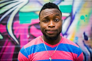 A man stands in front of a colourful graffiti wall, looking playfully confused.
