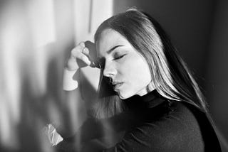 A woman holds her hand to her head with her eyes shut.