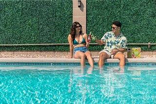 A guy and a girl sitting and relaxing with drinks in a swimming pool
