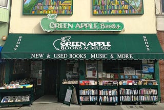 Green Apple Books and Music shop—a store with a green awning, a green neon sign, and cases of books on the sidewalk.