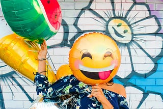 Woman holding smiling emoji ballon over face