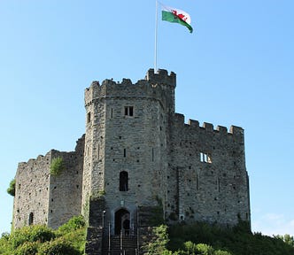 A castle keep with a Welsh flag (red dragon with white sky and green grass background) flying overhead