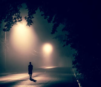 A long dark road, a man stands alone, creating a feeling of emptiness and lonliness.