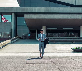A man in a suite leaving the office building looking at his mobile phone