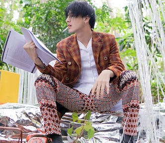 Stylish man reading a printed article while sitting on foil steps in his garden and smoking a cigarette