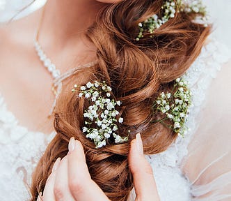 A young bride happily smiling, with flowers threaded through her hair.