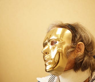 Picture of a woman wearing a golden mask which hides her features.