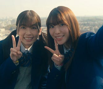 Two girls in school uniforms smile for a selfie while riding a Ferris Wheel.